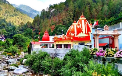 Brightly colored temple complex with a red and white dome next to a flowing river, surrounded by lush mountains